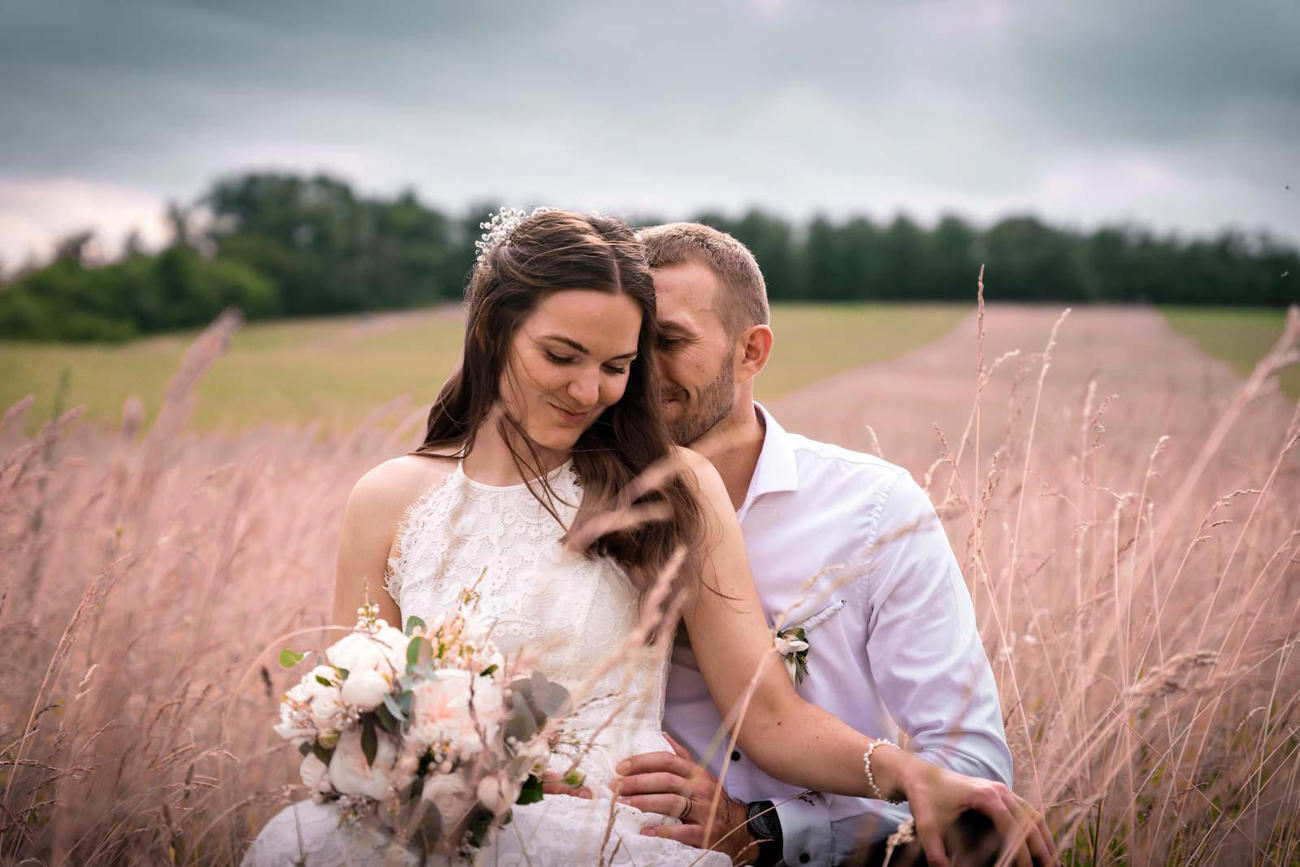 Nevěsta v bílých šatech s ženichem a květinou